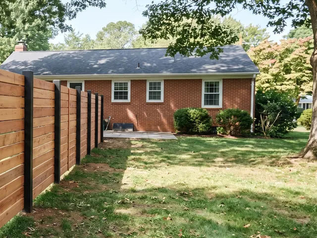 Detail view of A modern horizontal cedar-board fence with evenly spaced horizontal boards fixed across regularly spaced dark square posts in a leafy Charlottesville area setting