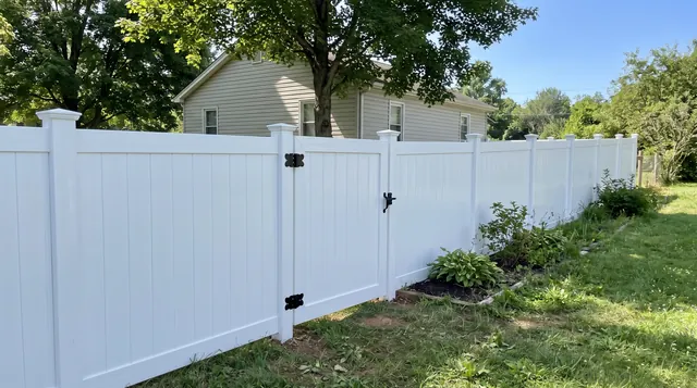 A clean white vinyl privacy fence with solid tongue-and-groove panels, capped square posts, bottom rails and a matching closed white walk gate in a leafy Stanardsville area setting