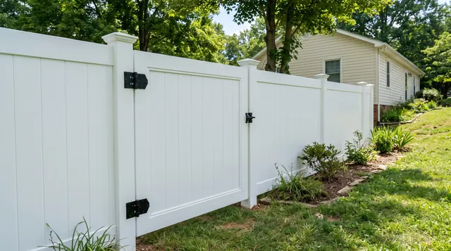 A close oblique view of a closed white vinyl walk gate in a matching white privacy fence, with visible black hinges and latch on capped square posts in a leafy Lovingston area setting